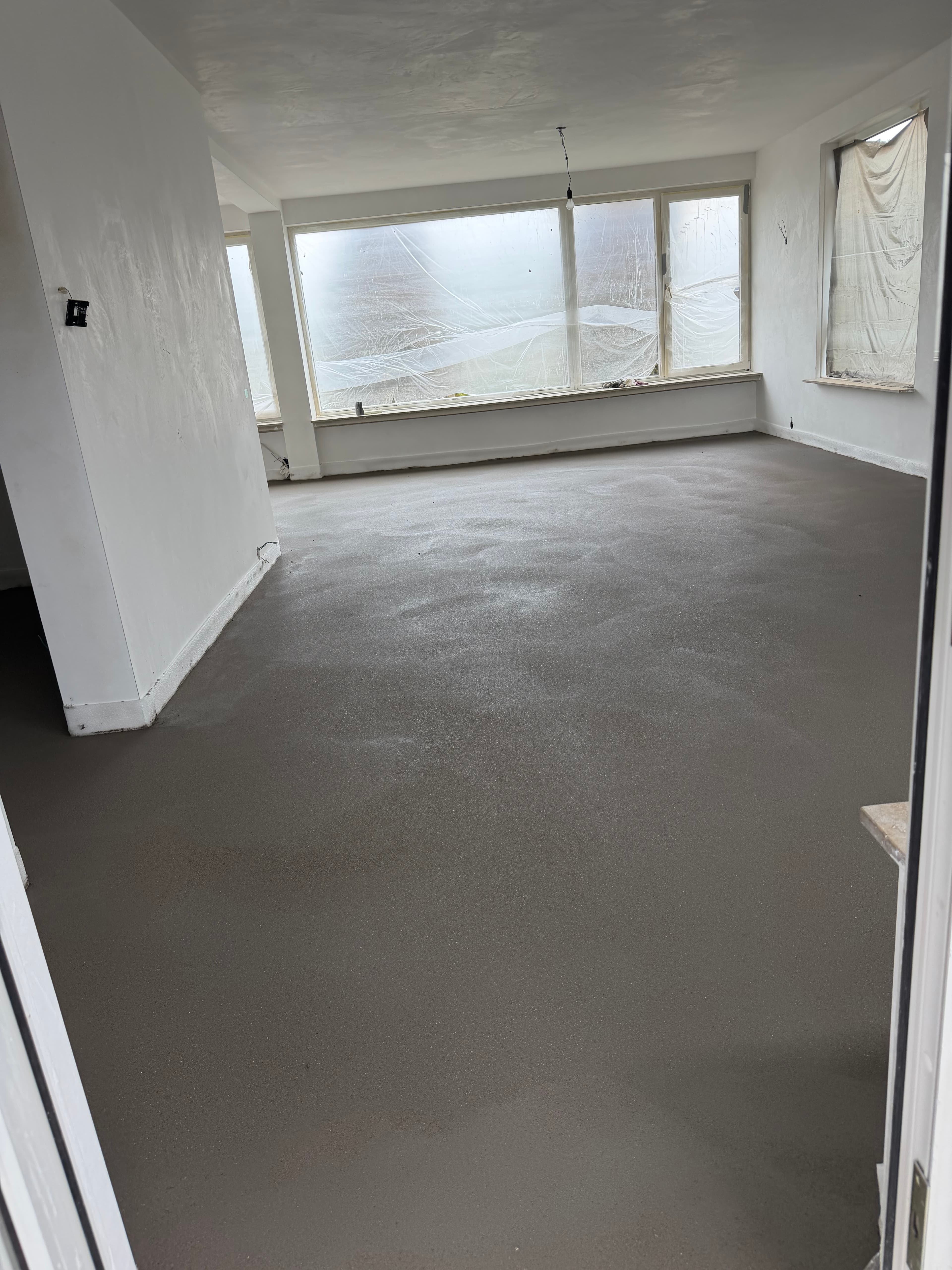 Een aangebrachte cementdekvloer in een woning met afgeplakte ramen